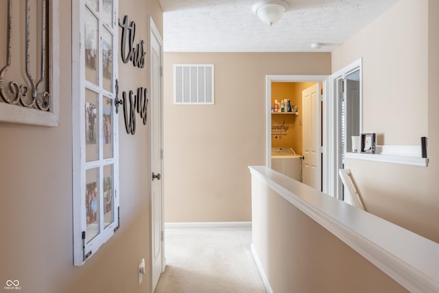 corridor featuring light colored carpet, a textured ceiling, and washer / clothes dryer