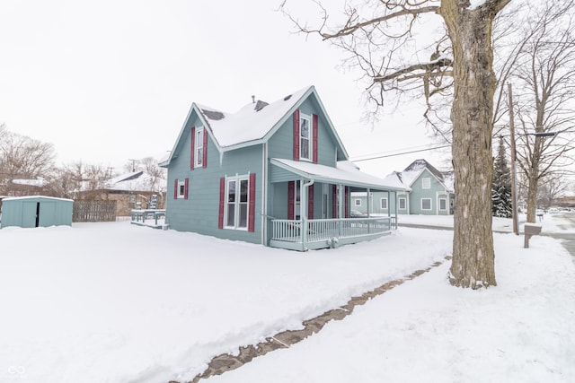 snow covered property featuring covered porch and a storage unit