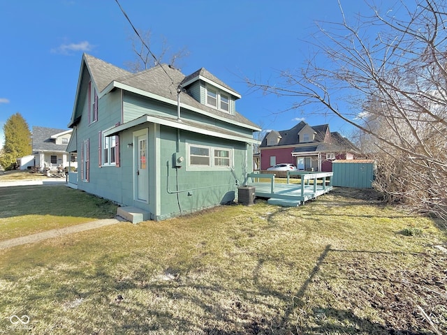 view of property exterior featuring a shingled roof, a deck, and a lawn