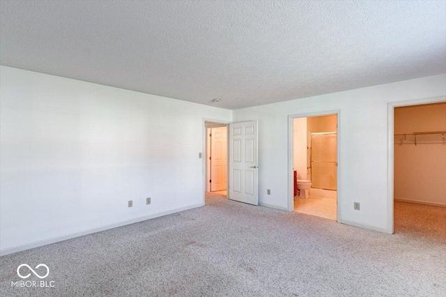 unfurnished bedroom featuring ensuite bath, a spacious closet, a textured ceiling, light colored carpet, and a closet