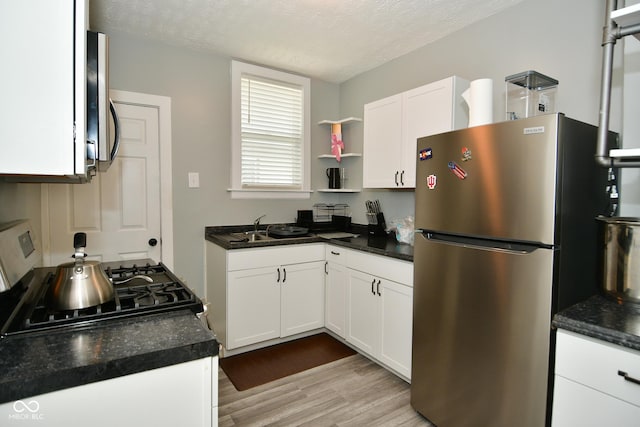 kitchen featuring white cabinets, stove, a textured ceiling, and stainless steel refrigerator