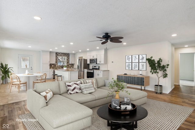 living room with dark wood-type flooring, ceiling fan, and a textured ceiling