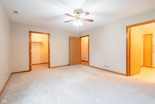 unfurnished bedroom with ceiling fan, a spacious closet, light carpet, and a closet