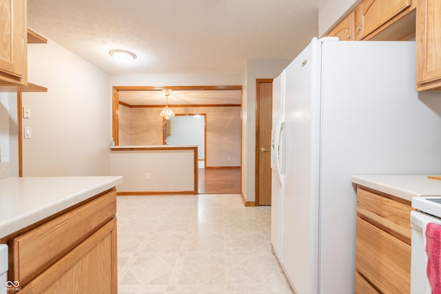 kitchen with a textured ceiling, white refrigerator with ice dispenser, hanging light fixtures, and light brown cabinetry