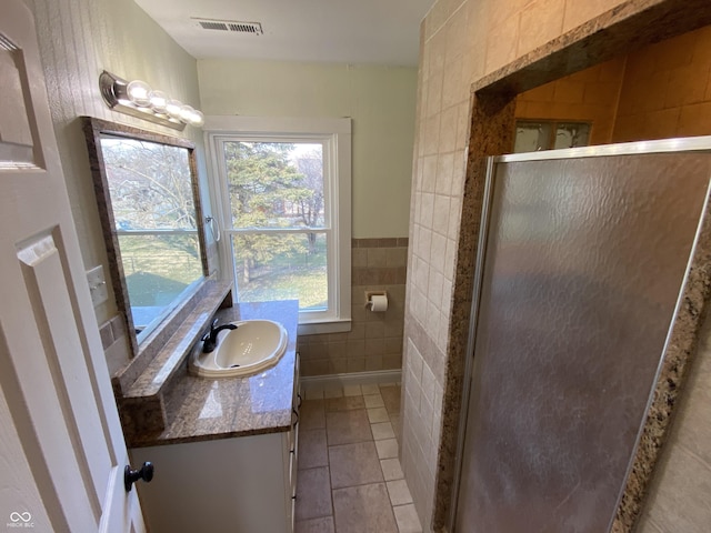 bathroom with tile patterned floors, vanity, a shower with shower door, and tile walls