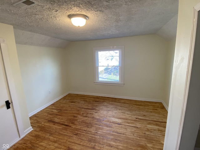 unfurnished room featuring a textured ceiling, hardwood / wood-style flooring, and lofted ceiling