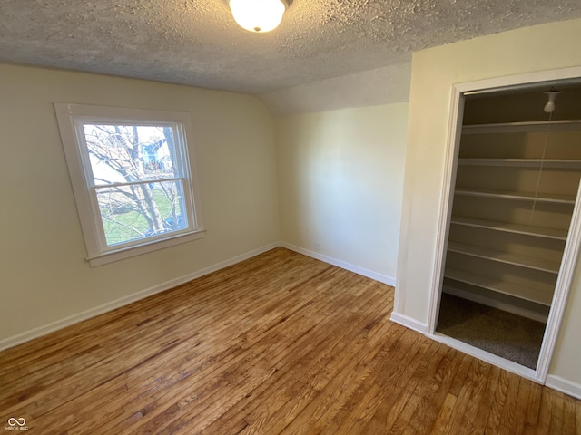 unfurnished bedroom featuring a textured ceiling, a closet, hardwood / wood-style floors, and lofted ceiling