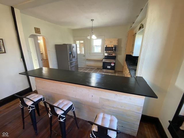 kitchen with kitchen peninsula, a kitchen bar, stainless steel appliances, dark hardwood / wood-style floors, and hanging light fixtures