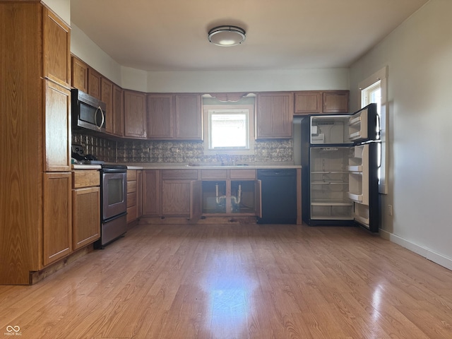 kitchen with appliances with stainless steel finishes, sink, backsplash, and light hardwood / wood-style flooring