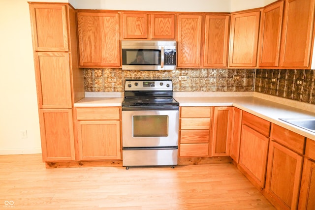 kitchen with stainless steel appliances, tasteful backsplash, sink, and light wood-type flooring