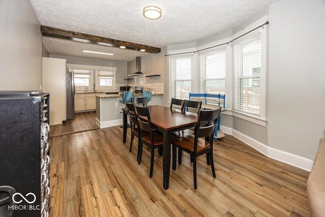 dining room with beamed ceiling, a textured ceiling, a wealth of natural light, and light hardwood / wood-style flooring