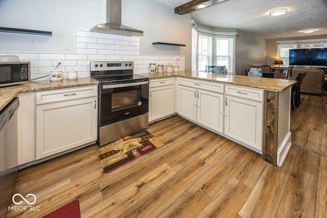 kitchen featuring wall chimney range hood, kitchen peninsula, light hardwood / wood-style floors, white cabinets, and appliances with stainless steel finishes