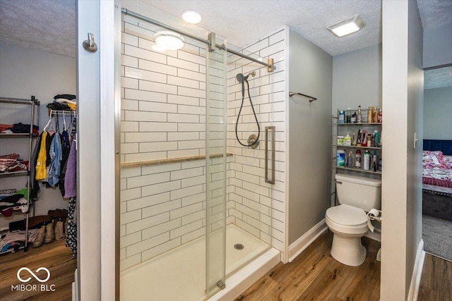 bathroom with a shower with shower door, toilet, wood-type flooring, and a textured ceiling