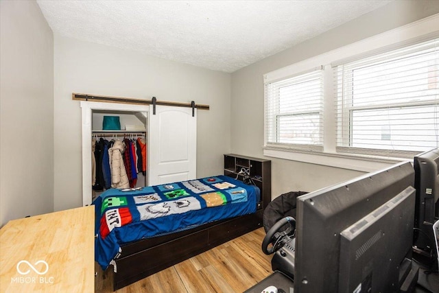 bedroom with wood-type flooring, a textured ceiling, a closet, and a barn door