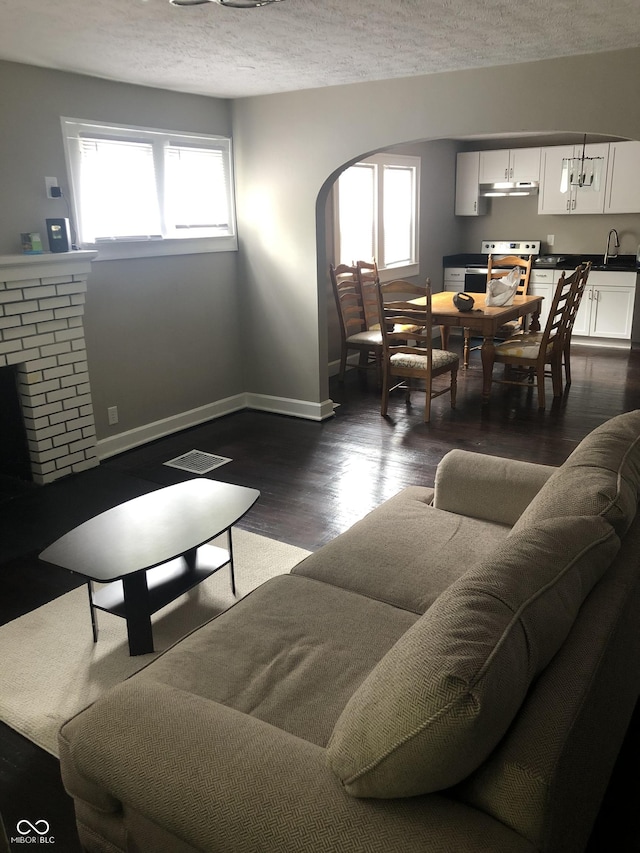 living room featuring a fireplace, a textured ceiling, dark wood-type flooring, and sink