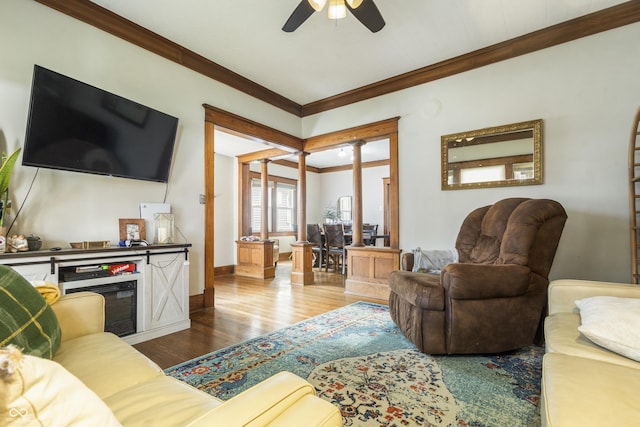 living room featuring decorative columns, ceiling fan, crown molding, and wood-type flooring