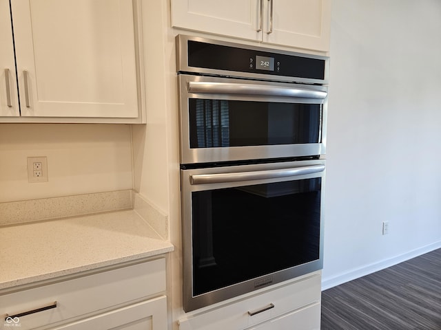 kitchen featuring double oven, light stone counters, white cabinetry, and dark hardwood / wood-style floors