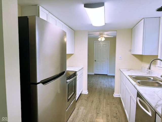 kitchen with light wood-type flooring, stainless steel appliances, ceiling fan, sink, and white cabinets