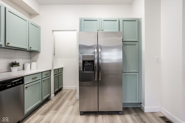 kitchen with decorative backsplash, light wood-type flooring, stainless steel appliances, and green cabinetry