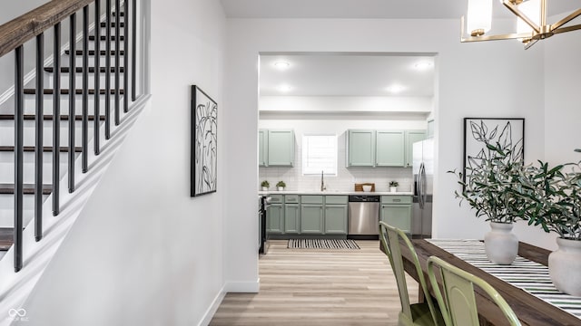 interior space with backsplash, light hardwood / wood-style floors, a chandelier, appliances with stainless steel finishes, and green cabinetry