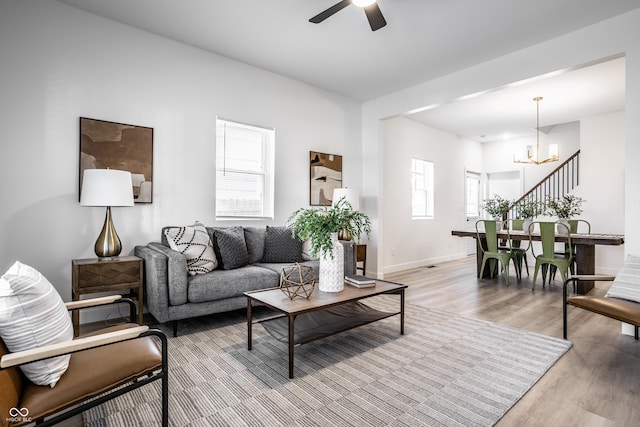 living room with ceiling fan with notable chandelier and light hardwood / wood-style flooring