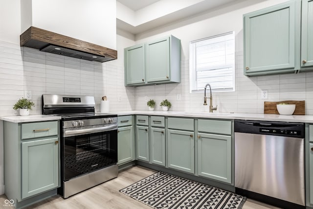 kitchen featuring custom exhaust hood, stainless steel appliances, sink, light hardwood / wood-style flooring, and green cabinetry