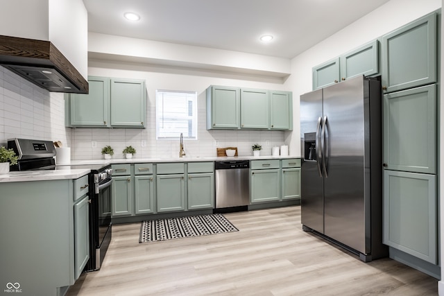 kitchen with green cabinets, sink, light wood-type flooring, custom range hood, and stainless steel appliances