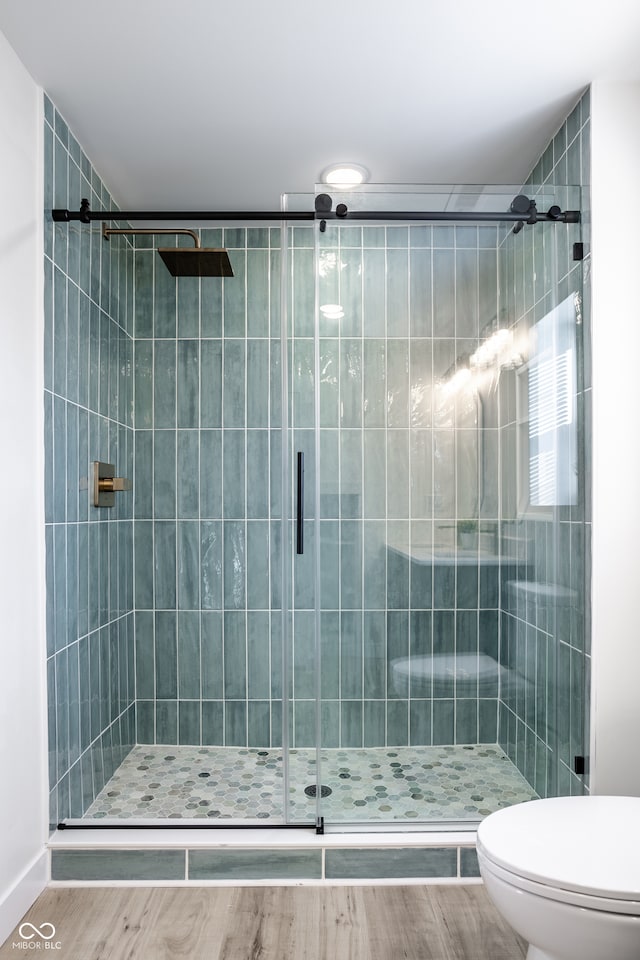 bathroom with hardwood / wood-style flooring, a shower with shower door, and toilet