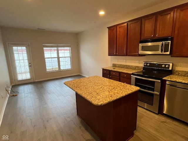 kitchen with light stone counters, light hardwood / wood-style flooring, a kitchen island, and appliances with stainless steel finishes