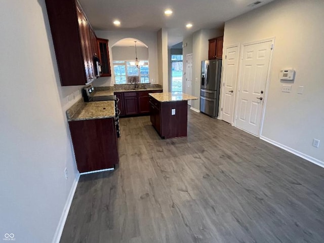 kitchen featuring an inviting chandelier, light stone counters, appliances with stainless steel finishes, a kitchen island, and dark hardwood / wood-style flooring