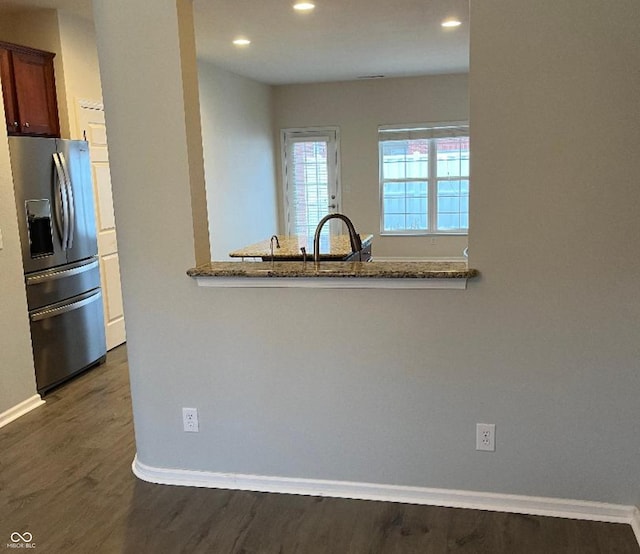 kitchen with light stone countertops, stainless steel fridge, dark hardwood / wood-style floors, and kitchen peninsula