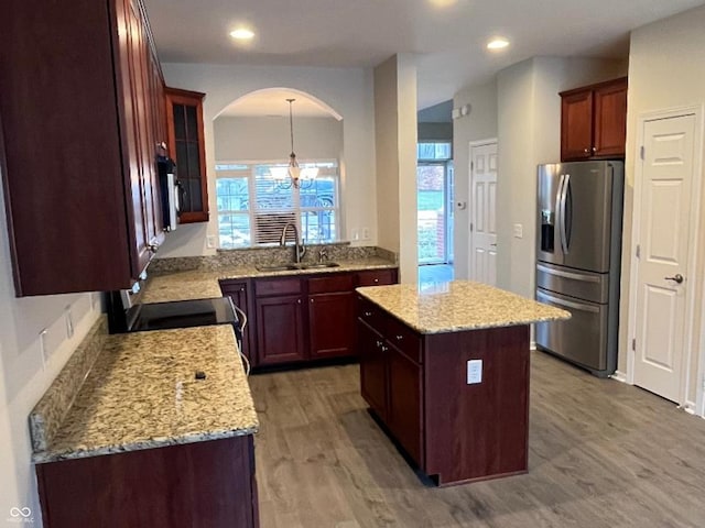 kitchen featuring light stone countertops, a center island, stainless steel refrigerator with ice dispenser, a notable chandelier, and wood-type flooring