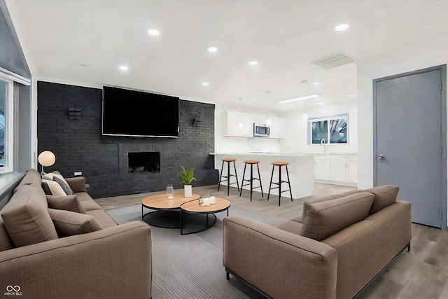 living room featuring sink, a fireplace, brick wall, and light wood-type flooring