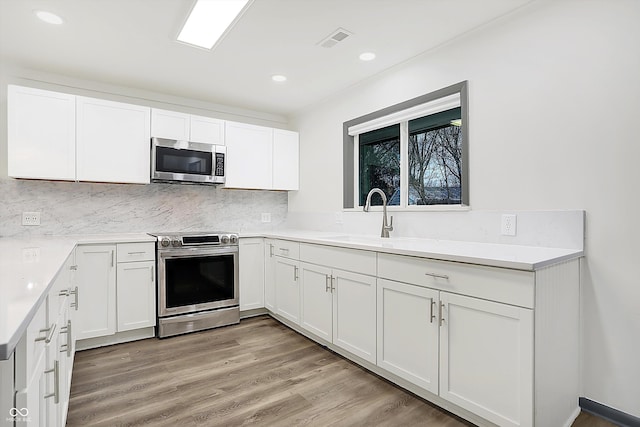 kitchen with sink, light hardwood / wood-style floors, decorative backsplash, white cabinets, and appliances with stainless steel finishes