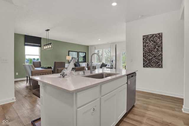 kitchen with a kitchen island with sink, sink, stainless steel dishwasher, decorative light fixtures, and white cabinetry