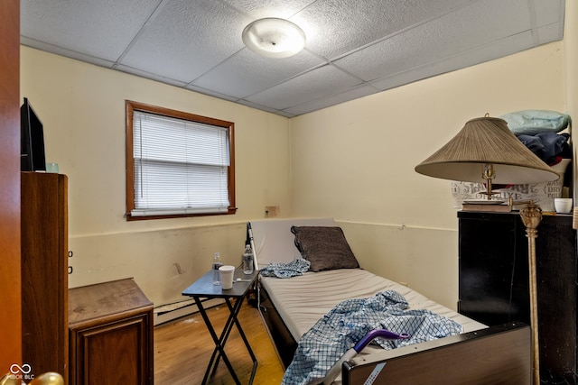 bedroom with hardwood / wood-style flooring, a drop ceiling, and baseboard heating