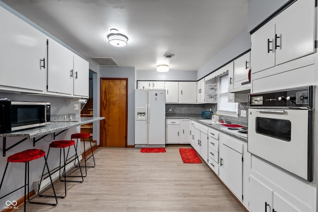 kitchen with a breakfast bar, tasteful backsplash, white appliances, light hardwood / wood-style floors, and white cabinets