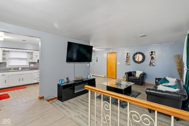 living room featuring sink, a baseboard radiator, and light wood-type flooring