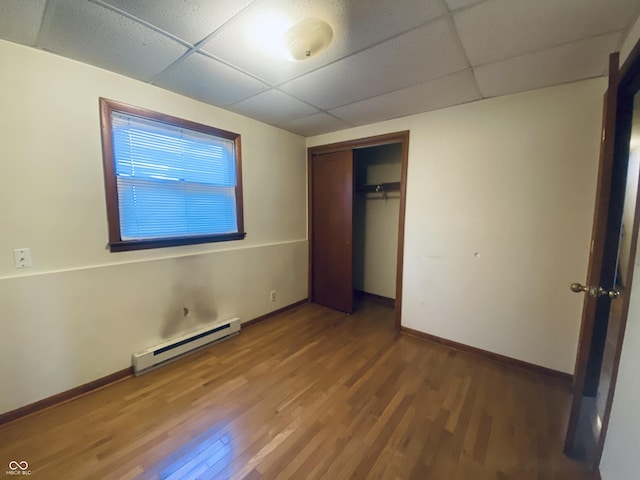 unfurnished bedroom featuring a baseboard radiator, hardwood / wood-style floors, a drop ceiling, and a closet