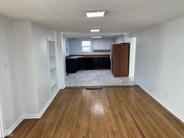 kitchen with dark brown cabinetry, dishwasher, sink, light hardwood / wood-style floors, and a textured ceiling