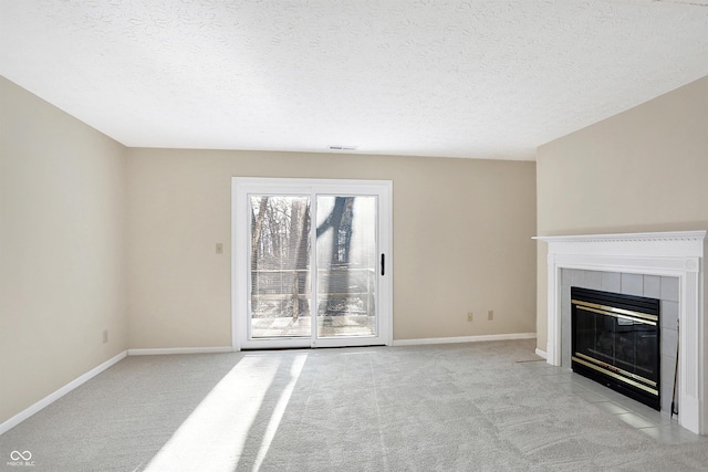 unfurnished living room featuring a tile fireplace, light carpet, and a textured ceiling