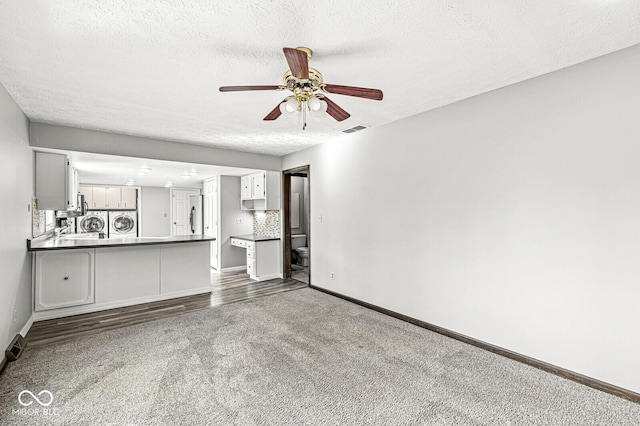 unfurnished living room featuring dark colored carpet, washer and dryer, ceiling fan, and a textured ceiling