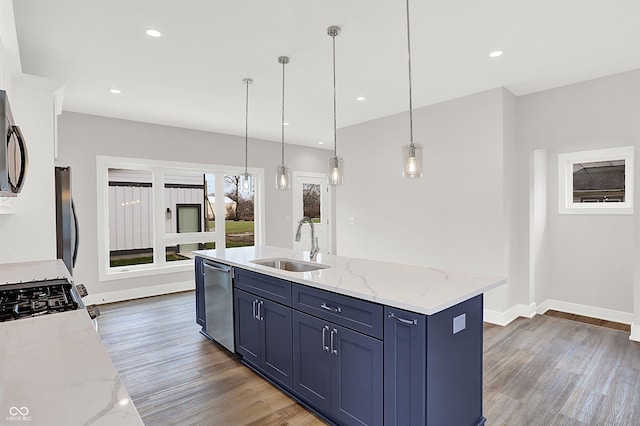 kitchen with light stone countertops, sink, stainless steel appliances, pendant lighting, and a center island with sink