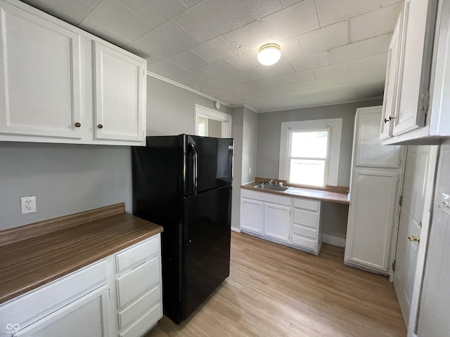 kitchen with black refrigerator, sink, built in desk, light hardwood / wood-style floors, and white cabinetry