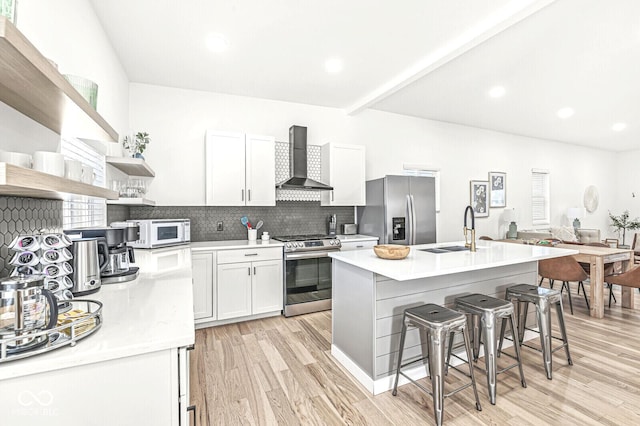 kitchen with appliances with stainless steel finishes, a kitchen breakfast bar, sink, wall chimney range hood, and white cabinets