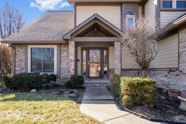 view of exterior entry with a shingled roof and brick siding