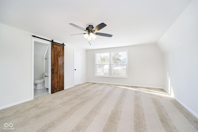 unfurnished bedroom featuring vaulted ceiling, ensuite bathroom, light colored carpet, ceiling fan, and a barn door