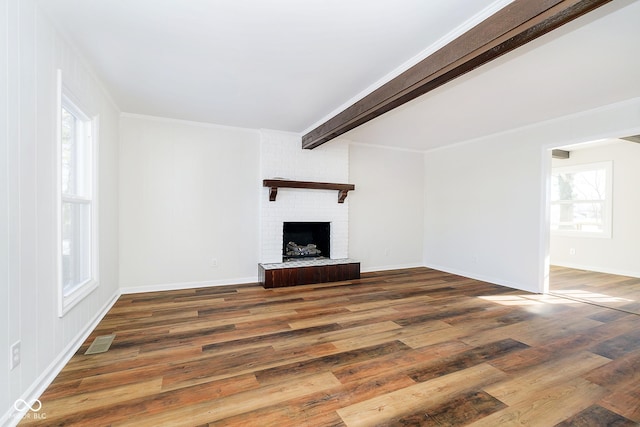 unfurnished living room featuring dark wood-type flooring, ornamental molding, a brick fireplace, and beamed ceiling