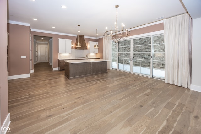 kitchen featuring pendant lighting, tasteful backsplash, light wood-type flooring, a kitchen island with sink, and white cabinets