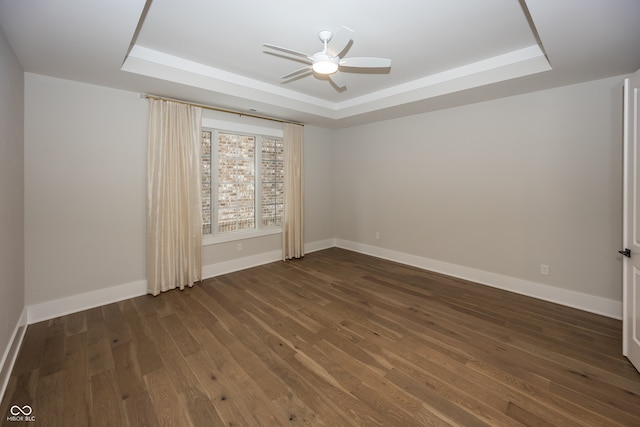 spare room with ceiling fan, dark wood-type flooring, and a tray ceiling